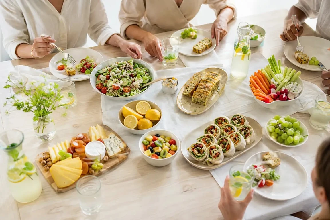 Repas froid entre amis avec buffet convivial de salades, wraps, cake salé et fruits frais sur grande table